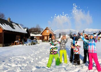 Ludzie w kolorowych strojach na ośnieżonej drodze wśród drewnianych domków. Traveligo Blog