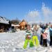 Ludzie w kolorowych strojach na ośnieżonej drodze wśród drewnianych domków. Traveligo Blog