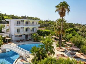 Biały budynek hotelowy z basenem i palmami. Traveligo Blog