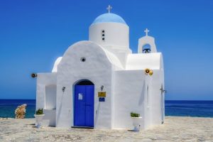 Biała, błękitna kaplica z kopułą przy brzegu morza. Traveligo Blog