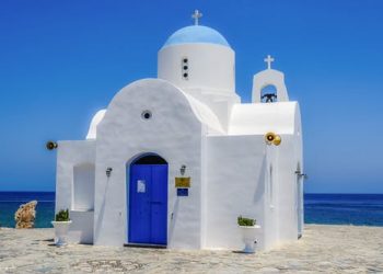 Biała, błękitna kaplica z kopułą przy brzegu morza. Traveligo Blog
