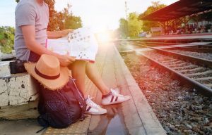 Kobieta siedzi na tle torów kolejowych, trzyma mapę - Traveligo Blog