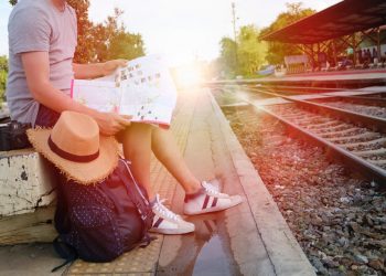 Kobieta siedzi na tle torów kolejowych, trzyma mapę - Traveligo Blog