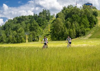 Zielona, górska sceneria z jazydącymi na rowerach ludźmi - Traveligo Blog