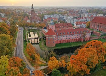 Stary, pomarańczowy zamek na tle jesiennej przyrody. Traveligo Blog