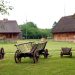 Drewniane domy z dachem ze strzechy. Stare kolorowe wozy zaprzęgowe. Trawnik. Traveligo Blog