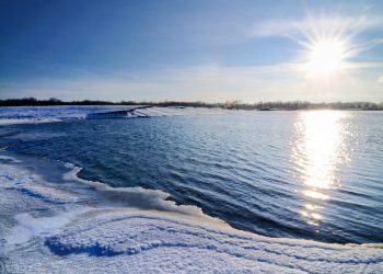 Zaśnieżona plaża nad rzeką przy wschodzącym słońcu. Traveligo Blog