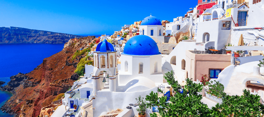 Panorama Santorini z białymi budynkami i niebieskimi kopułami kościołów nad lazurową wodą