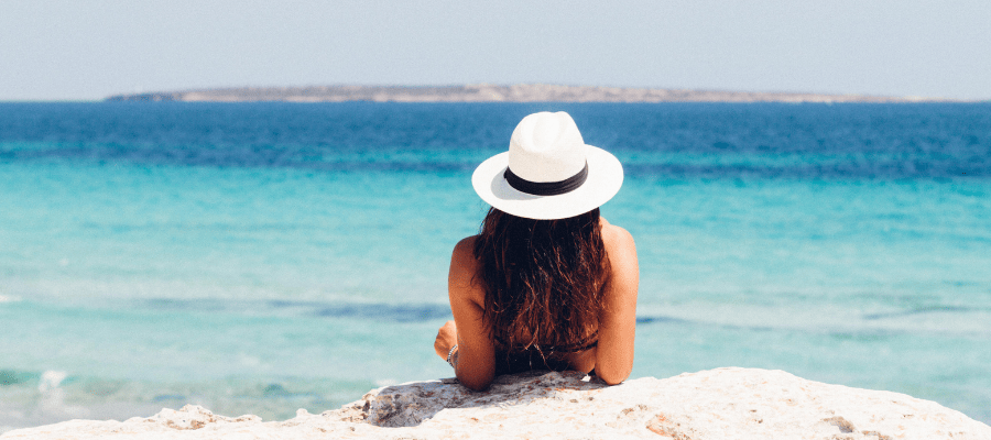 kobieta w kapeluszu odpoczywa na plaży z widokiem na turkusowe morze