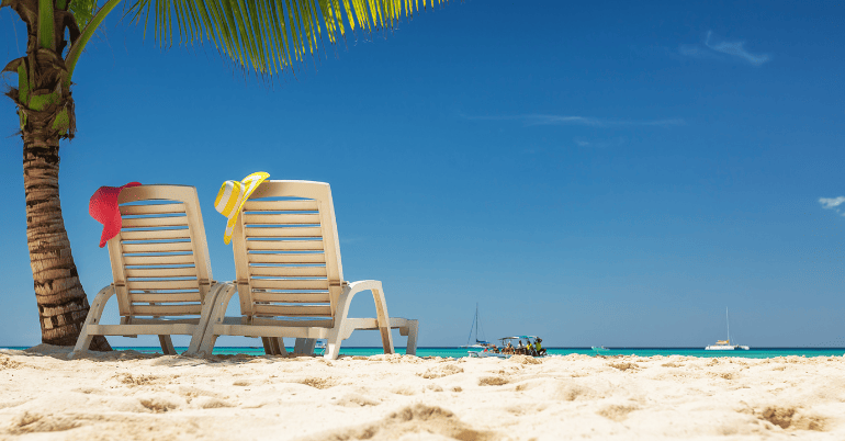 dwa leżaki pod palmą na białej, tropikalnej plaży z widokiem na morze