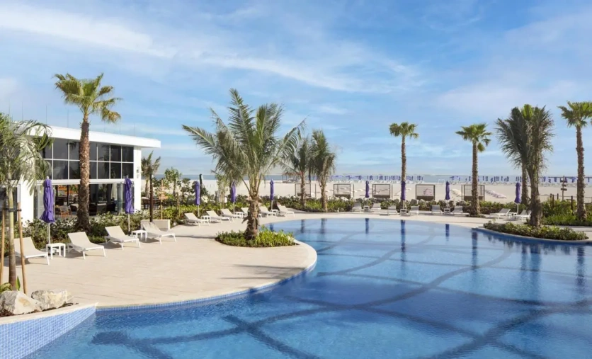Widok na basen, palmy i plażę w hotelu Centara Mirage Beach Resort Dubai z nowoczesną zabudową w tle