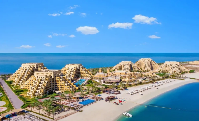 Panoramiczny widok na hotel Rixos Bab Al Bahr z charakterystycznymi piramidowymi budynkami, basenami i szeroką plażą nad zatoką