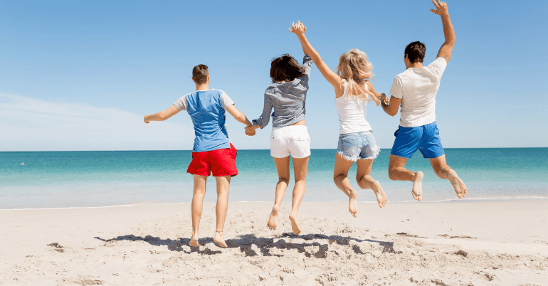 grupa osób skacze na plaży z widokiem na turkusowe morze