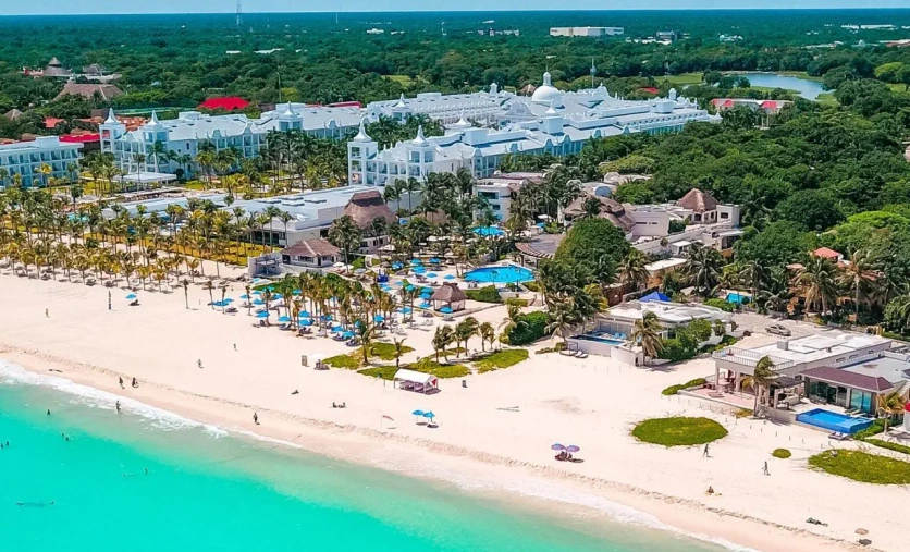 Widok z lotu ptaka na hotel The Reef Playacar Resort & Spa z tropikalną roślinnością, basenami i szeroką, białą plażą nad turkusowym morzem