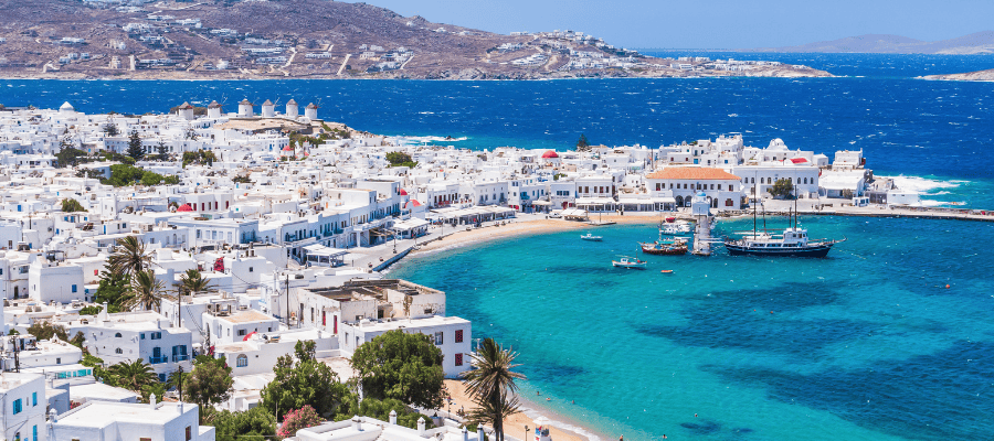 Widok na białe zabudowania Mykonos i turkusowe morze z charakterystycznymi wiatrakami w tle.