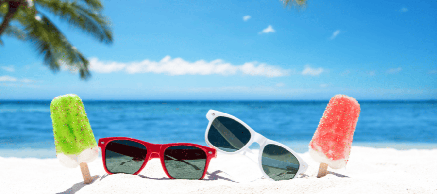 Kolorowe lody na patyku i okulary przeciwsłoneczne ustawione na białym piasku tropikalnej plaży.