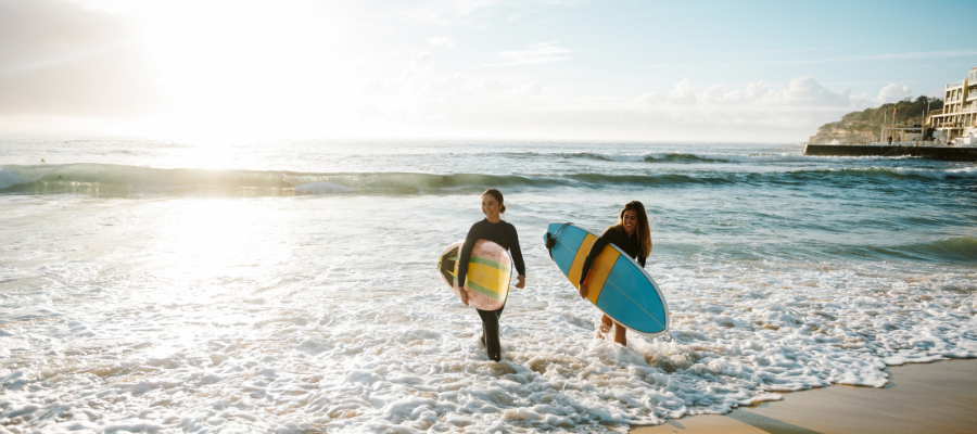 Dwie osoby z deskami surfingowymi na plaży o zachodzie słońca – egzotyka zima 2027